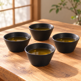Four Japanese black ceramic tea cups filled with tea on a wooden table