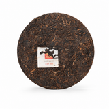Unwrapped 2023 BESTLEAFTEA Ancient Tree Ripe Pu-erh tea cake showing compressed dark tea leaves and center label on a white background