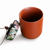 Yixing Zisha clay tea caddy with decorative floral fabric pouch beside a matching travel tea cup
