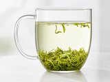 Glass mug of brewed green tea with loose tea leaves at the bottom