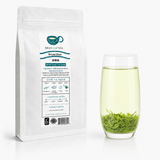 White pouch of Bi Luo Chun green tea beside a glass of brewed tea with leaves at the bottom