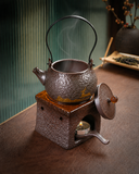 Mini gongfu teapot with candle warmer on tea table beside glass pitcher of golden tea
