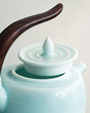 Close-up of the teapot lid and curved wooden handle on celadon Qingbai porcelain