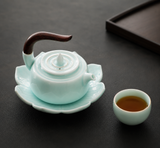 Celadon Qingbai porcelain teapot with lotus-shaped saucer and wooden handle on dark tabletop