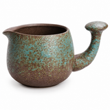 Handmade speckled green ceramic tea pitcher with brown interior and textured green glaze on a clean white background

