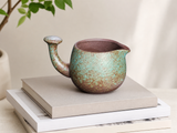 Handmade speckled green ceramic tea pitcher displayed on stacked books in a minimalist lifestyle setting