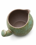 Close-up of handmade speckled green ceramic tea pitcher showing the open spout, brown interior, and textured glaze