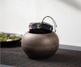 Rustic coarse pottery tea canister with fabric lid partially open, showing loose tea leaves inside in a traditional tea setting.