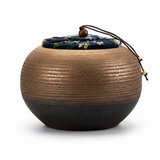 Rustic coarse pottery tea canister with floral fabric lid on a clean white background, showing textured ceramic craftsmanship.