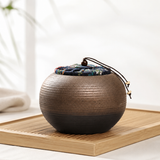 Rustic ceramic tea canister with floral fabric lid on a wooden tea tray, highlighting handcrafted texture and tea room style.