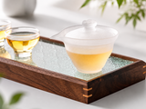 Frosted glass gaiwan with golden tea on a wooden tea tray with glass teacups, featuring a premium translucent design for elegant tea service.