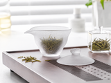 Frosted glass gaiwan with loose green tea leaves on a modern tea tray, showing the matte translucent glass finish and elegant gongfu tea setup.