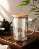 Borosilicate glass brewing mug with bamboo lid on a wooden tea tray in a calm tea lifestyle setting.