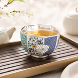 Silver-plated tea cup filled with amber tea on a wooden tea tray, highlighting the reflective interior and octagonal shape.