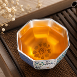 Silver-plated tea cup with amber tea on a wooden tea tray, showcasing an octagonal shape, reflective silver interior, and decorative floral enamel patterns.