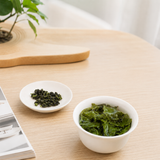 Loose Tie Guan Yin oolong tea leaves in a white cup and brewed leaves in another cup