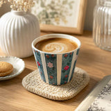 Blue striped ceramic coffee cup with raised floral relief, shown filled with latte on a table