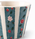 Close-up of hand-painted ceramic coffee cup with blue stripes and raised pink rose details