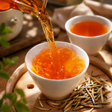 Black tea being poured into a white cup with golden tea buds on a wooden tray