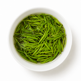 Fresh Zhu Ye Qing green tea leaves steeping in a white gaiwan on a minimalist white background