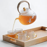 Glass teapot pouring tea into cups on bamboo tray, Japanese tea set