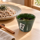 Styled serving suggestion with the green noodle dipping cup holding sauce beside soba noodles; food and accessories not included
