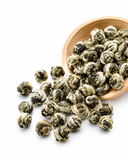 Close-up of hand-rolled Jasmine Pearl Green Tea pearls spilling from wooden scoop on white background